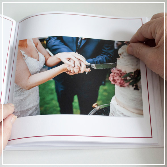 Gast klebt zu Hause ein Foto in sein Gastgeschenkbuch, zu sehen ist ein Foto und links und rechts wird jeweils eine Ecke mit den Händen gehalten